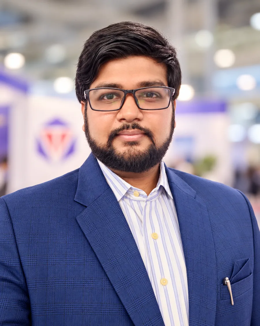 Angad Kulkarni, smiling, in a blue checked blazer at an industry expo